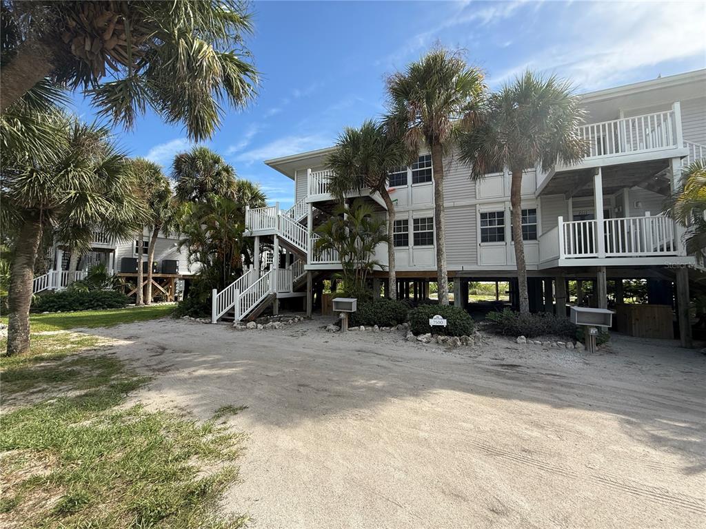 An exterior view of a multi-story, light-colored building on stilts with palm trees and sand — 7500 PLACIDA ROAD UNIT 2124, PLACIDA, FL