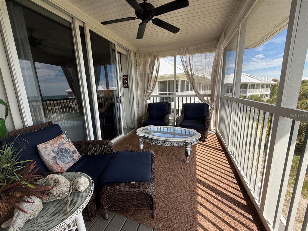 A screened-in porch features wicker furniture, a ceiling fan, and views of nearby coastal buildings — 7500 PLACIDA ROAD UNIT 2124, PLACIDA, FL