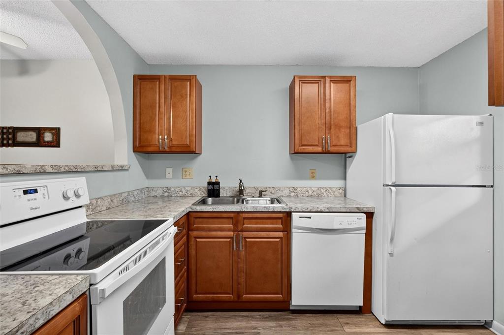 A kitchen features wood cabinets, white appliances, and a granite countertop with a sink — 640 N NOVA ROAD UNIT 209, ORMOND BEACH, FL