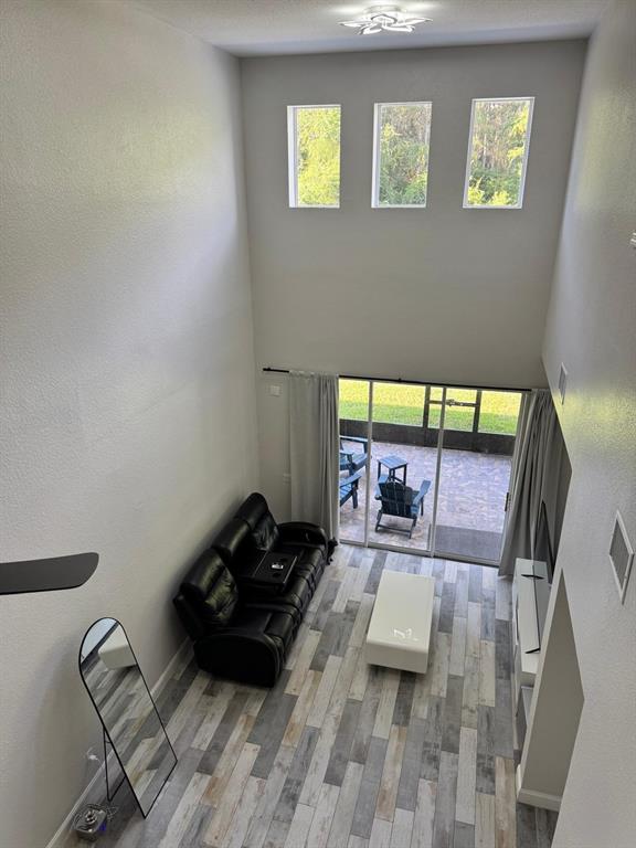 A high-ceilinged living room features wood-look tile flooring, a black sofa, and sliding glass doors — 1609 CROYDON STREET, ORLANDO, FL