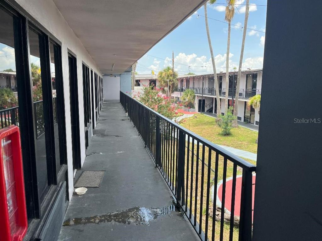 An outdoor walkway with a black metal railing overlooks a courtyard with palm trees — 8421 S ORANGE BLOSSOM TRAIL UNIT 263, ORLANDO, FL