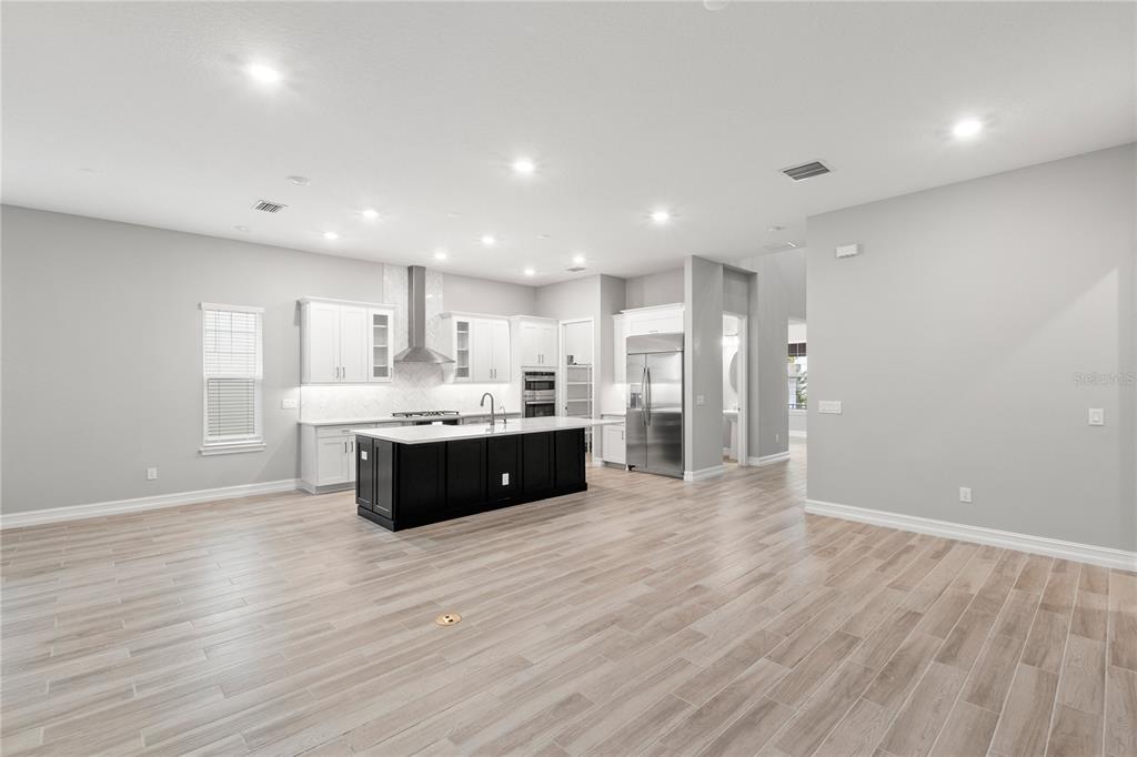A modern kitchen features white cabinetry, a dark island, and light wood-look tile flooring — 1011 SEAGRAPE DRIVE, RUSKIN, FL