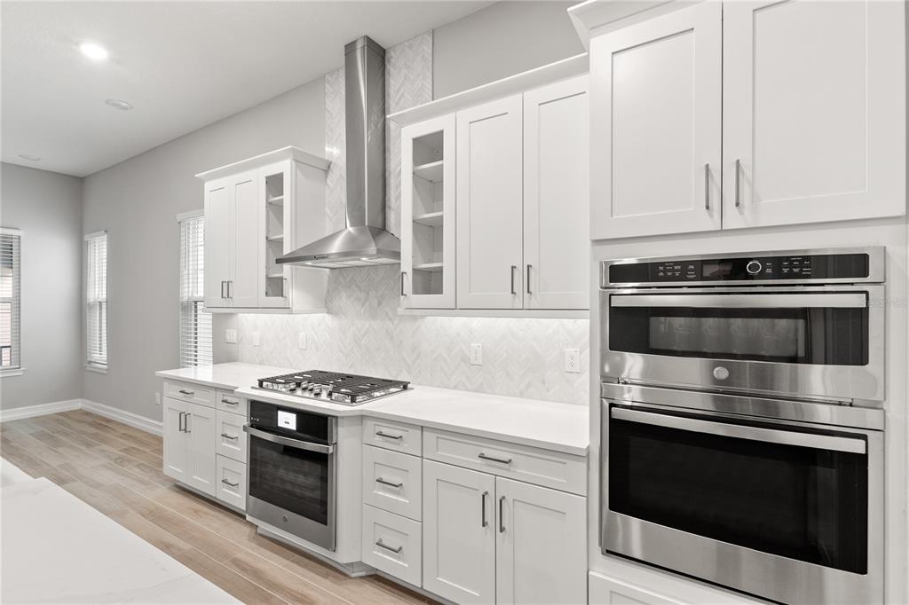 A modern kitchen features white cabinetry, stainless steel appliances, and a herringbone tile backsplash — 1011 SEAGRAPE DRIVE, RUSKIN, FL