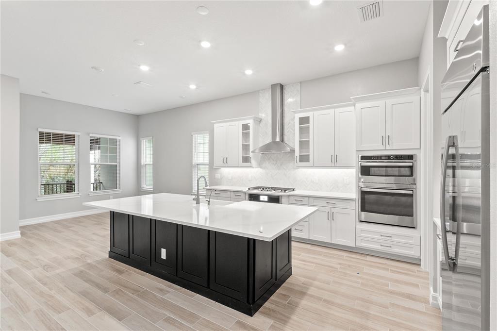 A modern kitchen features white cabinetry, a dark island, stainless steel appliances, and light flooring — 1011 SEAGRAPE DRIVE, RUSKIN, FL