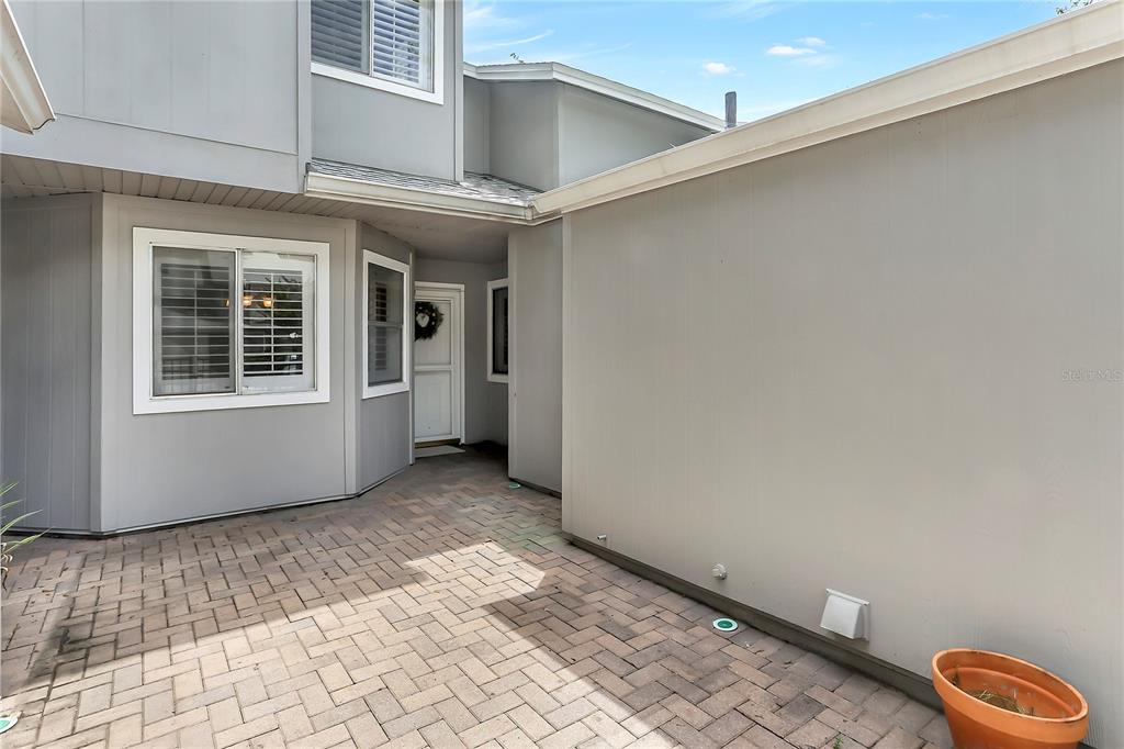A paved courtyard leads to the front entrance of a gray-sided two-story house — 605 CHESTNUT OAK CIRCLE UNIT 107, ALTAMONTE SPRINGS, FL