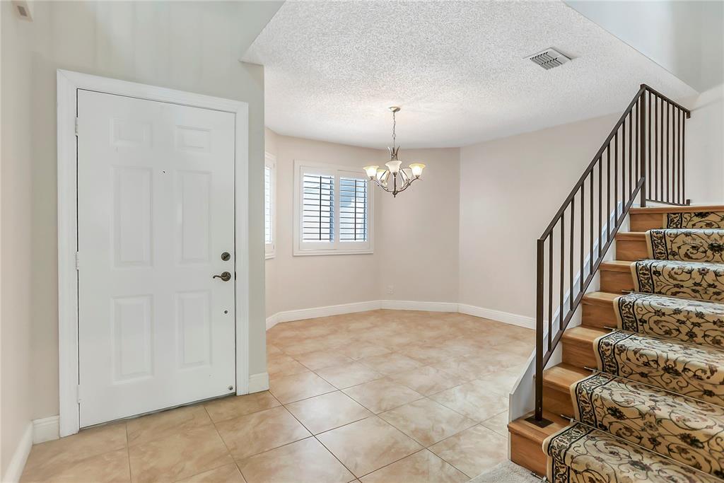 An entryway features tile flooring, a chandelier, a white front door, and a carpeted staircase — 605 CHESTNUT OAK CIRCLE UNIT 107, ALTAMONTE SPRINGS, FL