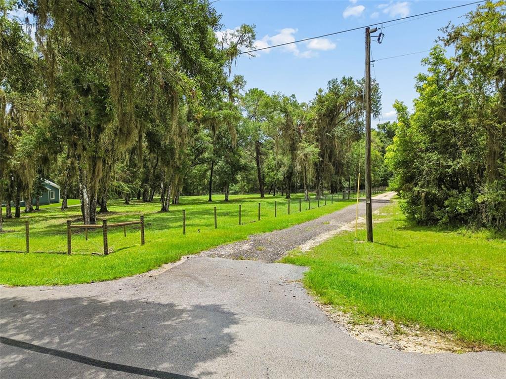 A gravel driveway leads into a grassy, tree-lined lot bordered by a wooden fence — 5111 E UNNAMED LANE, FLORAL CITY, FL