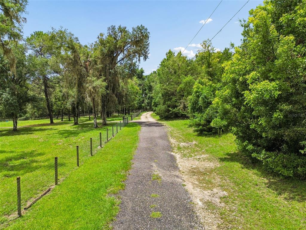 A gravel driveway leads through a grassy, tree-lined lot with a wire fence on the left — 5111 E UNNAMED LANE, FLORAL CITY, FL