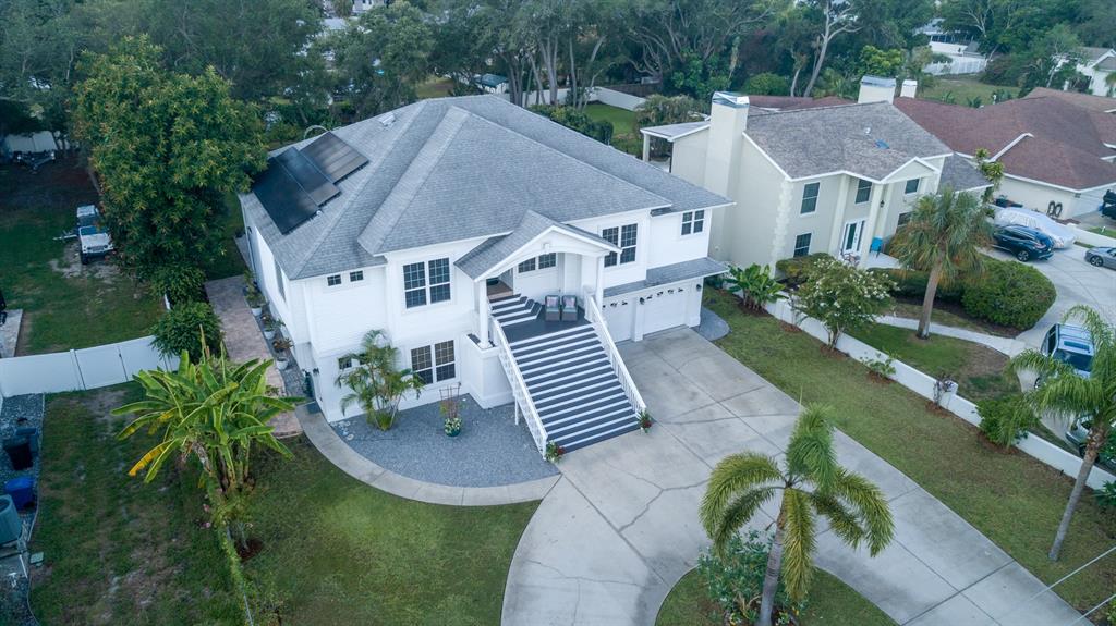 An elevated two-story house with a prominent staircase, solar panels, and a concrete driveway — 1605 GULF ROAD, TARPON SPRINGS, FL