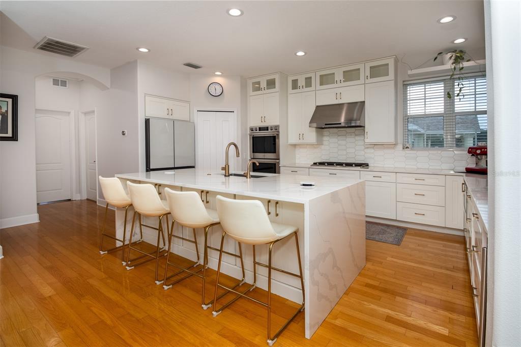 A modern kitchen features a large white quartz island, stainless steel appliances, and hardwood floors — 1605 GULF ROAD, TARPON SPRINGS, FL