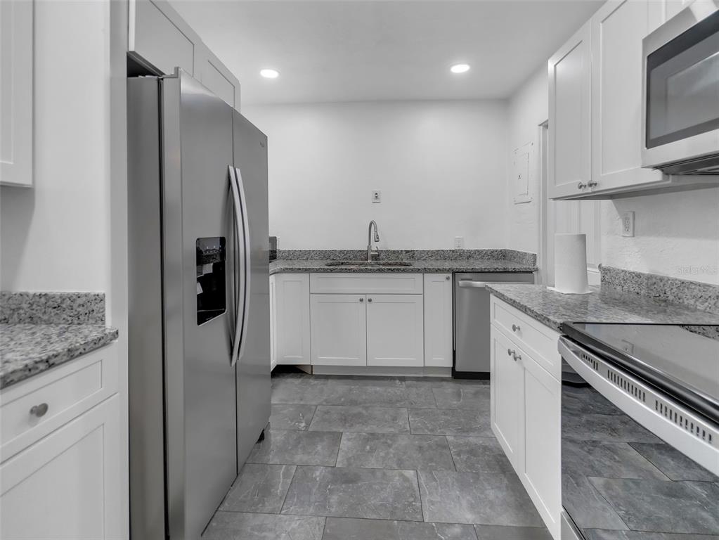 A kitchen features white cabinets, granite countertops, stainless steel appliances, and gray tile flooring — 2600 EUSTON ROAD, WINTER PARK, FL