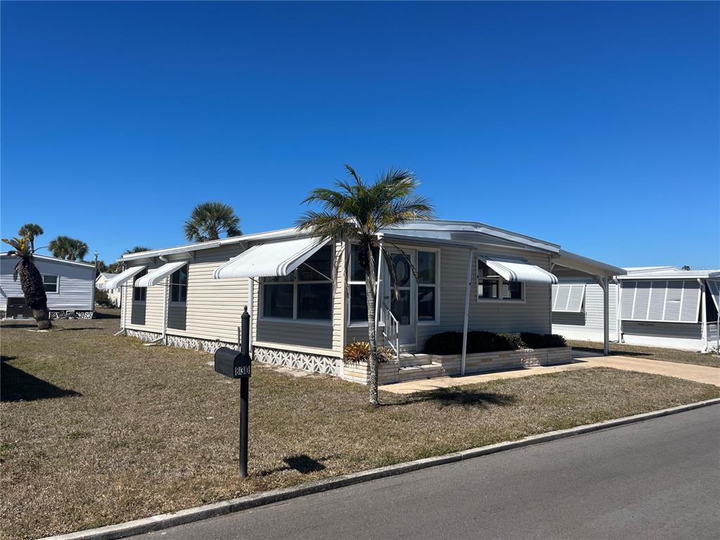 A single-story manufactured home with light siding, metal awnings, and a palm tree in front — 828 TRENTO, VENICE, FL