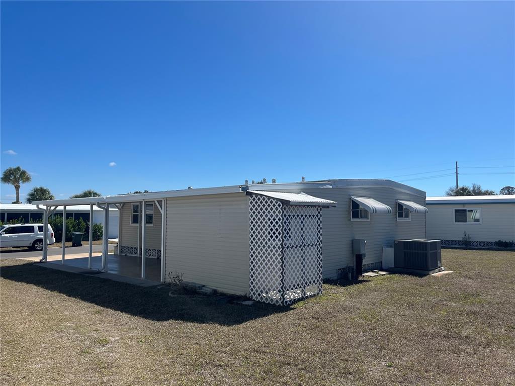 The exterior of a mobile home features a covered patio, lattice screen, and central air unit — 828 TRENTO, VENICE, FL
