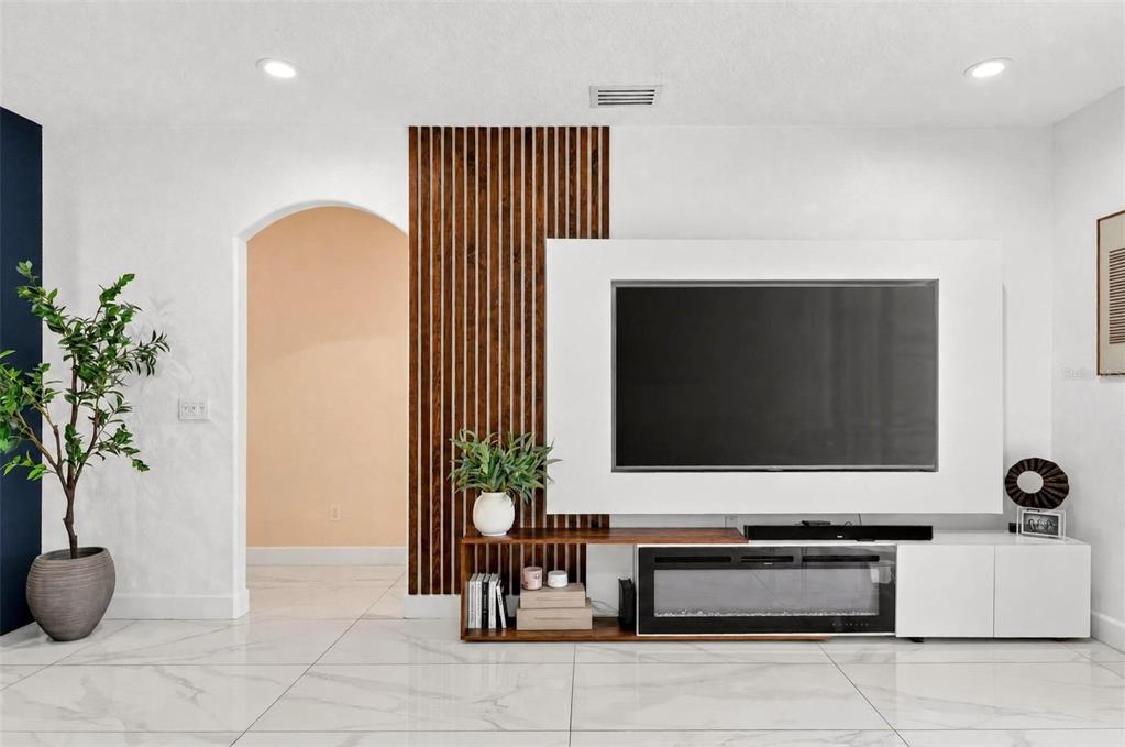 A living room features a wall-mounted television, a slatted wood accent wall, and a fireplace console — 3016 CAMINO REAL DRIVE S, KISSIMMEE, FL