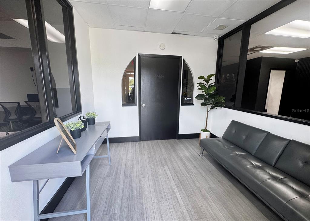 A waiting area features gray wood-look flooring, a black sofa, a console table, and windows — 120 W CARROLL STREET, KISSIMMEE, FL