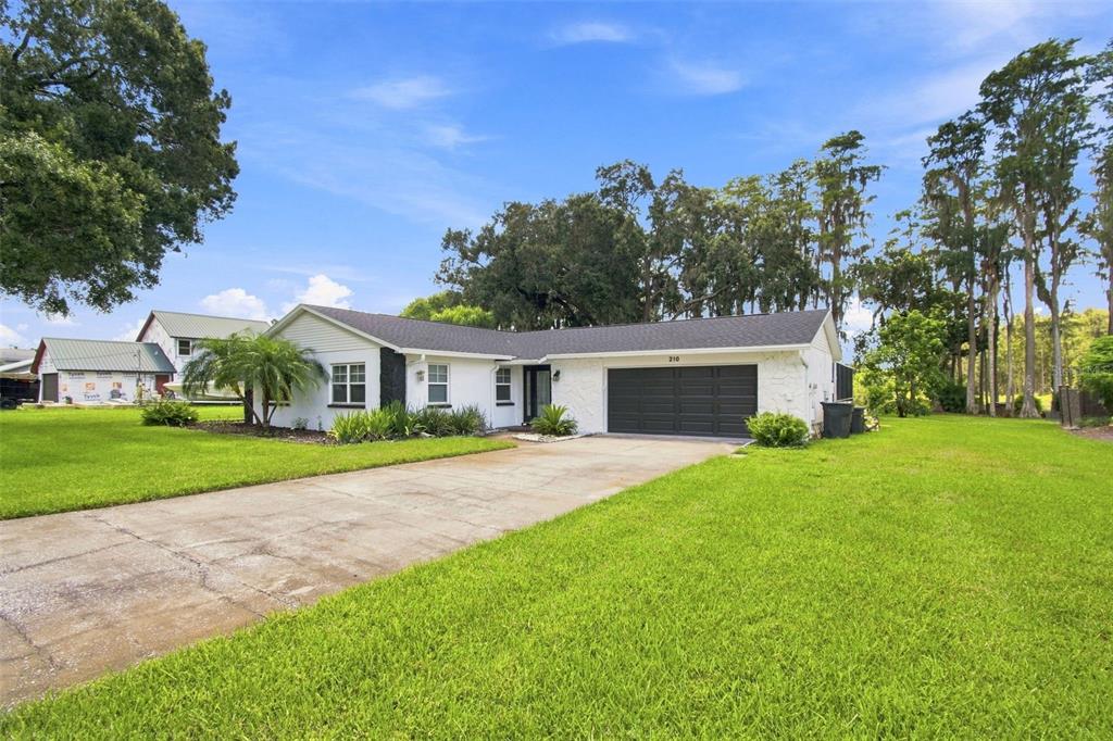 A single-story white house with a dark garage door and a concrete driveway — 210 LAKE HOBBS ROAD, LUTZ, FL