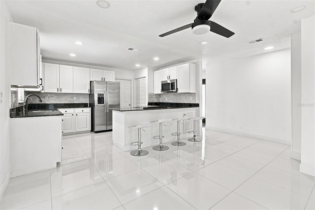 A modern kitchen features white cabinets, black countertops, stainless steel appliances, and white tile flooring — 210 LAKE HOBBS ROAD, LUTZ, FL