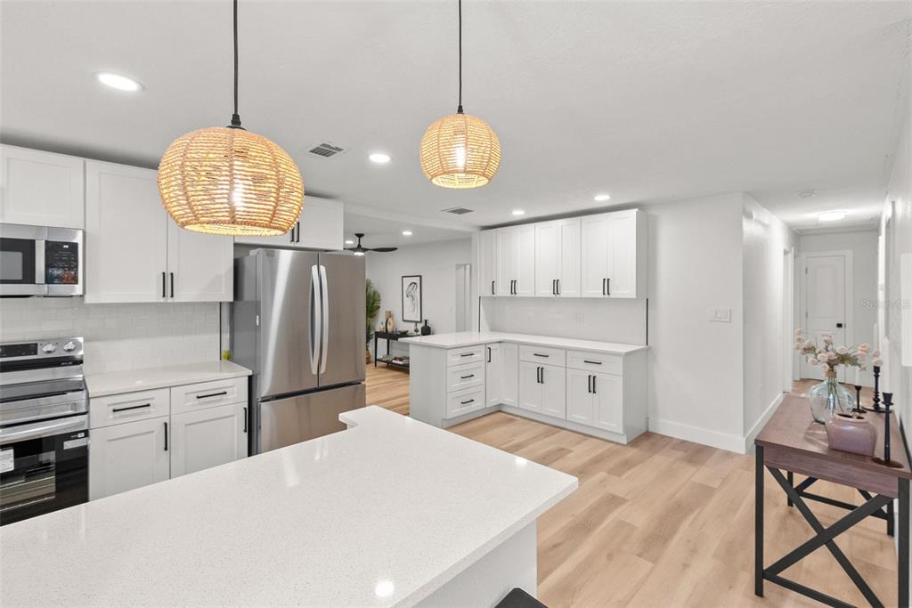 A modern kitchen features white cabinetry, stainless steel appliances, quartz countertops, and two woven pendant lights — 2312 22ND AVENUE SW, LARGO, FL