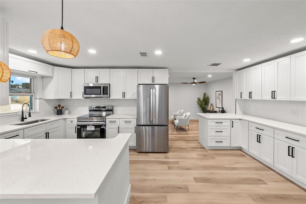 A modern kitchen features white cabinetry, stainless steel appliances, quartz countertops, and light wood flooring — 2312 22ND AVENUE SW, LARGO, FL