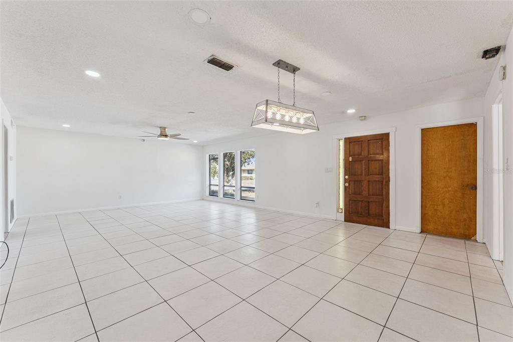 A bright, open-concept living area features white tile flooring, white walls, and a rectangular chandelier — 1457 MAGELLAN CIRCLE UNIT 1003, ORLANDO, FL