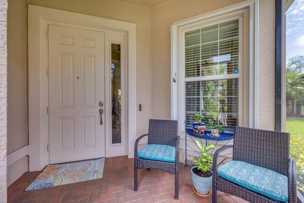 A covered entryway features a white front door, a window, and two chairs on pavers — 15824 AMBER FALLS DRIVE, WIMAUMA, FL