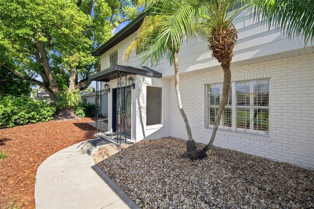 A white brick house exterior features a covered entryway, a palm tree, and gravel landscaping — 2705 SILVER LAKE AVENUE, TAMPA, FL