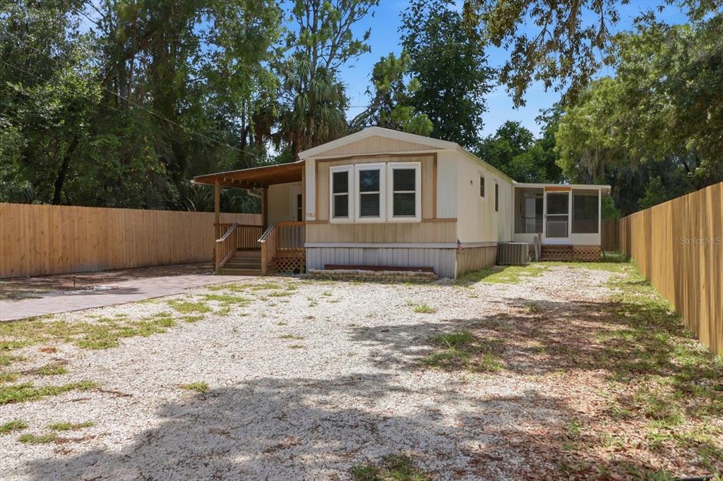 A single-story manufactured home with a gravel driveway, wooden porch, and fenced yard — 3496 S ARUNDEL TERRACE, HOMOSASSA, FL