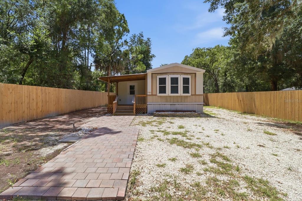 A single-story mobile home with a front porch, brick walkway, and wooden privacy fence — 3496 S ARUNDEL TERRACE, HOMOSASSA, FL