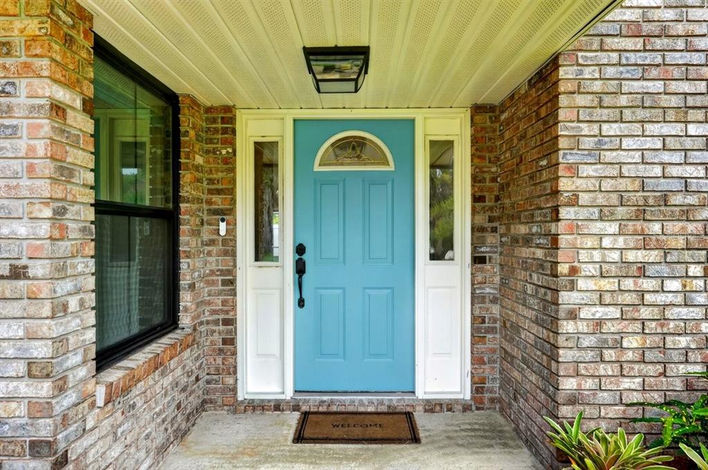 A light blue front door with sidelights is centered between two brick walls under a porch — 3 FOX HOLLOW DRIVE, ORMOND BEACH, FL