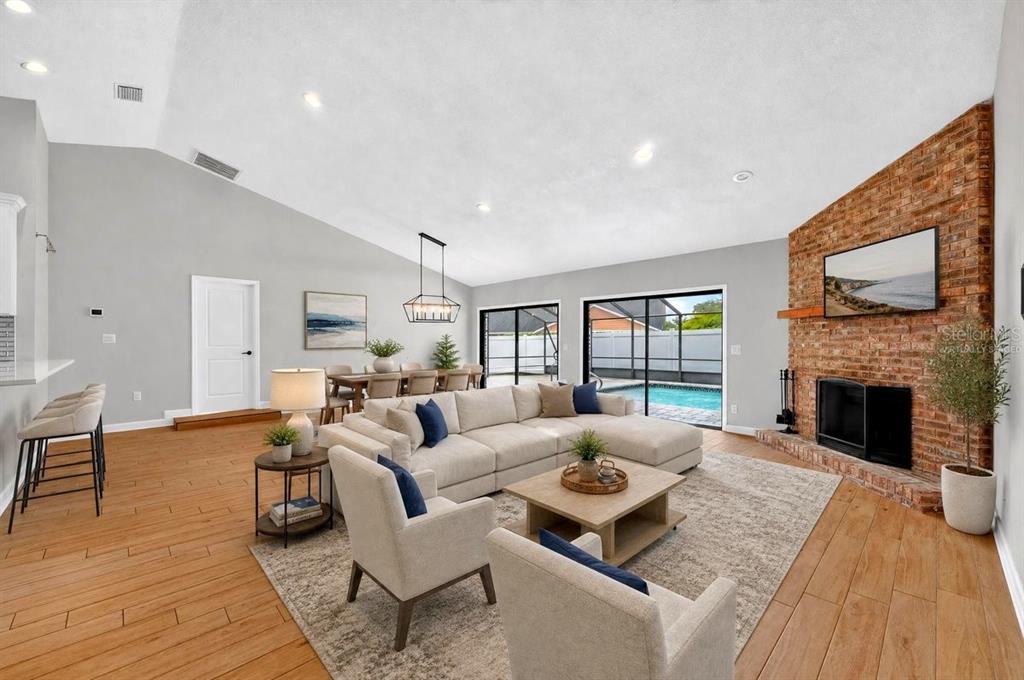 A living room with a brick fireplace, vaulted ceilings, and sliding doors opening to a pool — 3 FOX HOLLOW DRIVE, ORMOND BEACH, FL