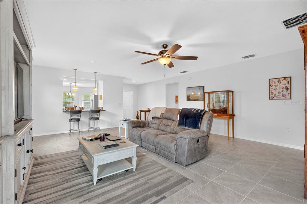 A living room features a grey sofa, a coffee table, and a pass-through to the kitchen — 5349 SANDPINE HAVEN LANE, PORT ORANGE, FL