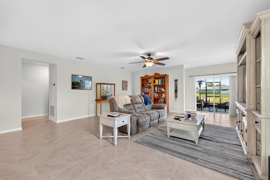 A living room features tile flooring, a brown sofa, a wooden bookcase, and sliding glass doors — 5349 SANDPINE HAVEN LANE, PORT ORANGE, FL