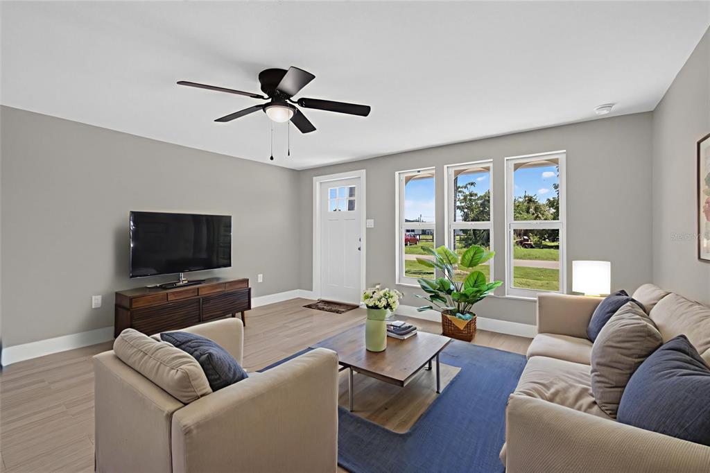 A living room features light gray walls, wood-look tile flooring, a ceiling fan, and large windows — 312 READING STREET NW, PORT CHARLOTTE, FL