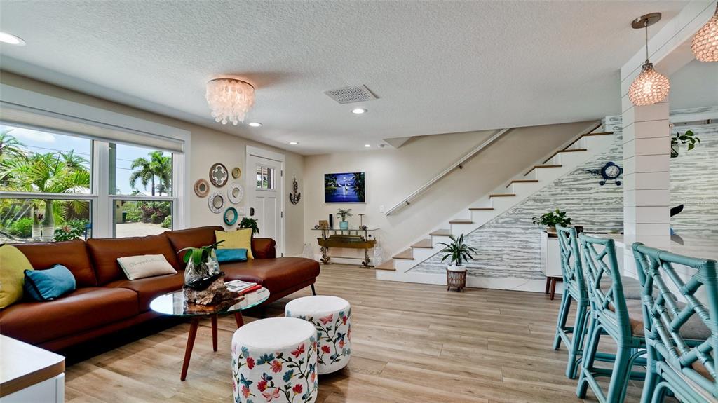 A living room features a brown leather sofa, stairs with shiplap walls, and teal chairs — 522 68TH STREET, HOLMES BEACH, FL