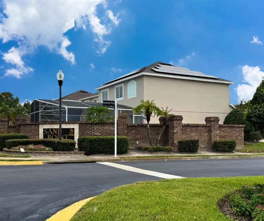 A blue two-story house with solar panels sits behind a brick wall and landscaping — 1203 SANDESTIN WAY, ORLANDO, FL