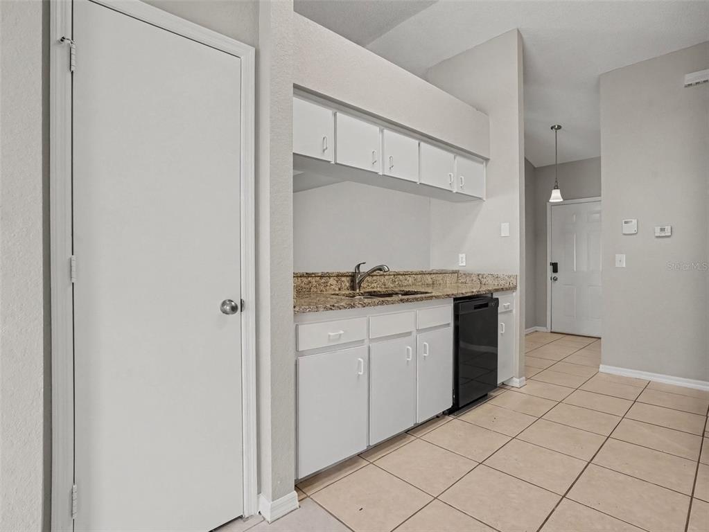 A kitchen features white cabinets, granite countertops, a black dishwasher, and light-colored tile flooring — 3735 IMPERIAL DRIVE, WINTER HAVEN, FL