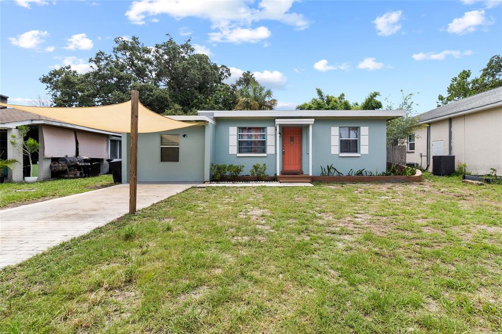 A single-story house with a light blue exterior, orange front door, and a tan shade sail — 5410 14TH AVENUE S, GULFPORT, FL