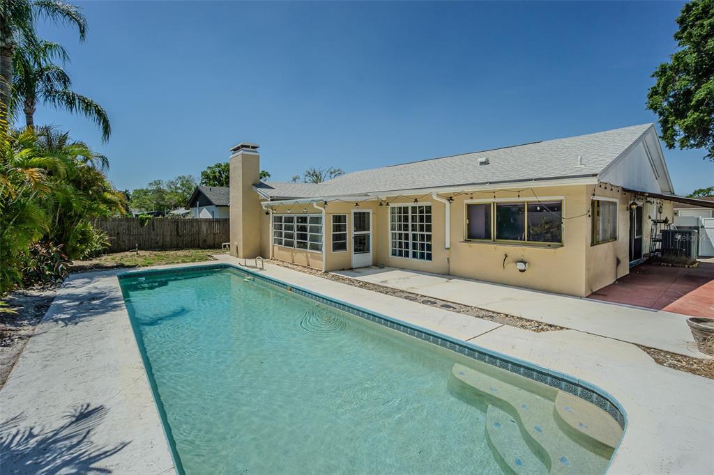 A backyard features a rectangular swimming pool with steps next to a single-story beige house — 7348 BROOKVIEW CIRCLE, TAMPA, FL