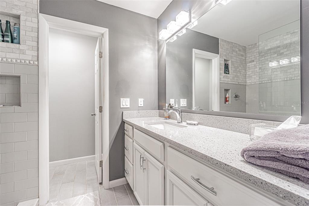 A bathroom features a gray vanity with a speckled countertop, a large mirror, and tiled walls — 7348 BROOKVIEW CIRCLE, TAMPA, FL