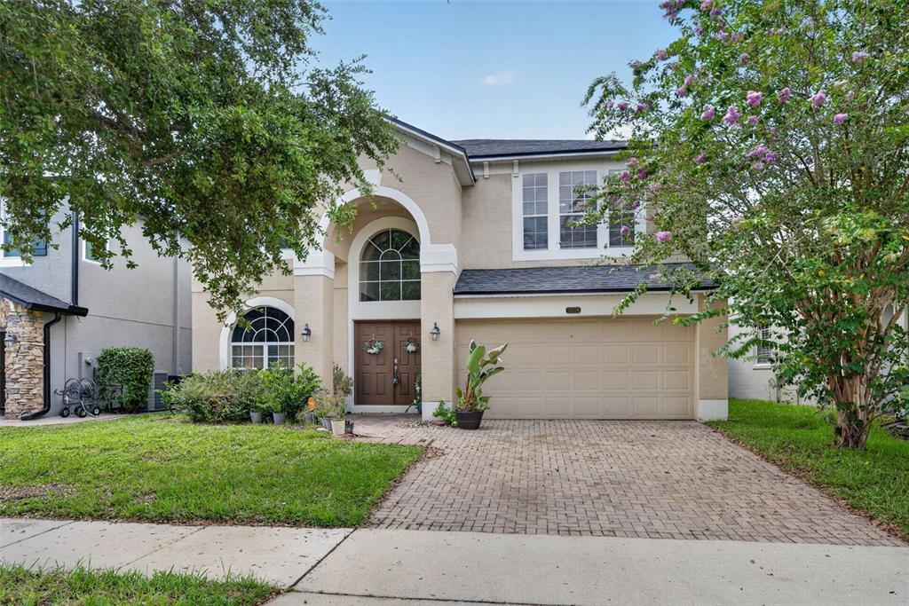 A two-story suburban house with a beige stucco exterior, arched windows, and a paved driveway — 13026 MOSS PARK RIDGE DRIVE, ORLANDO, FL