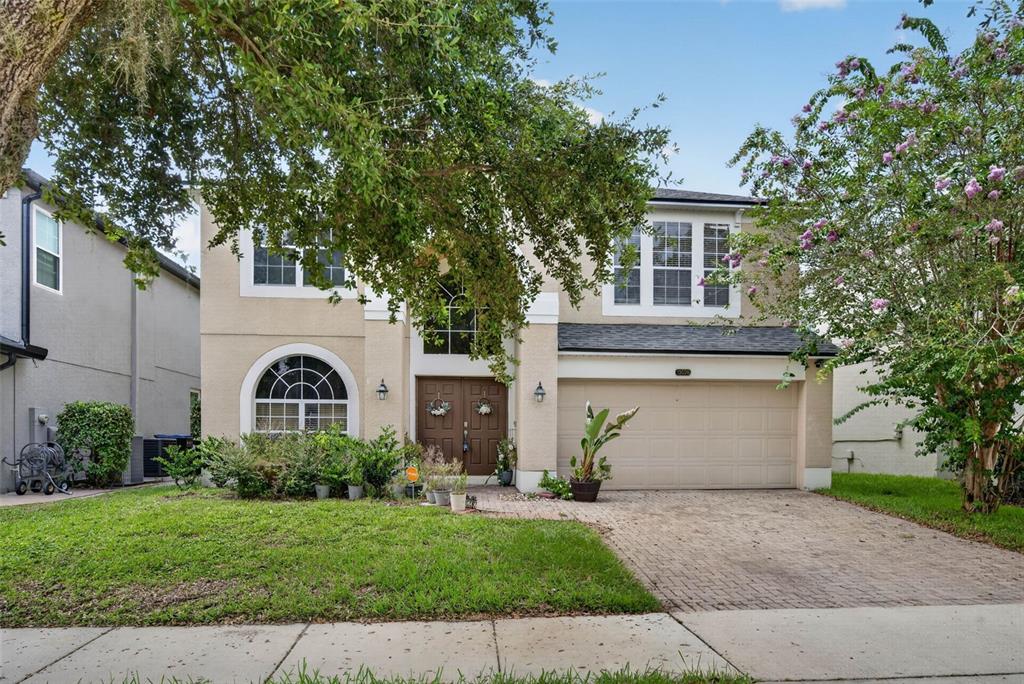 A two-story beige house with a brick driveway, arched window, and a two-car garage — 13026 MOSS PARK RIDGE DRIVE, ORLANDO, FL