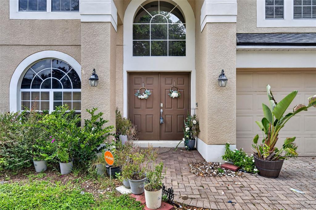 The exterior of a two-story home features a double front door, arched windows, and landscaping — 13026 MOSS PARK RIDGE DRIVE, ORLANDO, FL