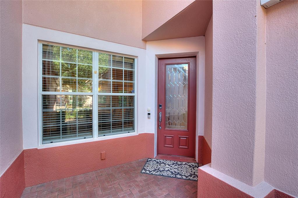 A red front door with a glass insert sits beside a window on a patio — 1411 LISBON CT, DAVENPORT, FL