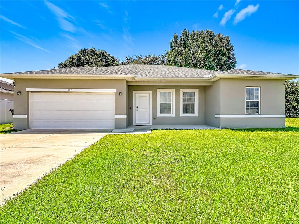 A single-story house with a white garage door, a front entrance, and a green lawn — 306 CLEARWATER LANE, POINCIANA, FL