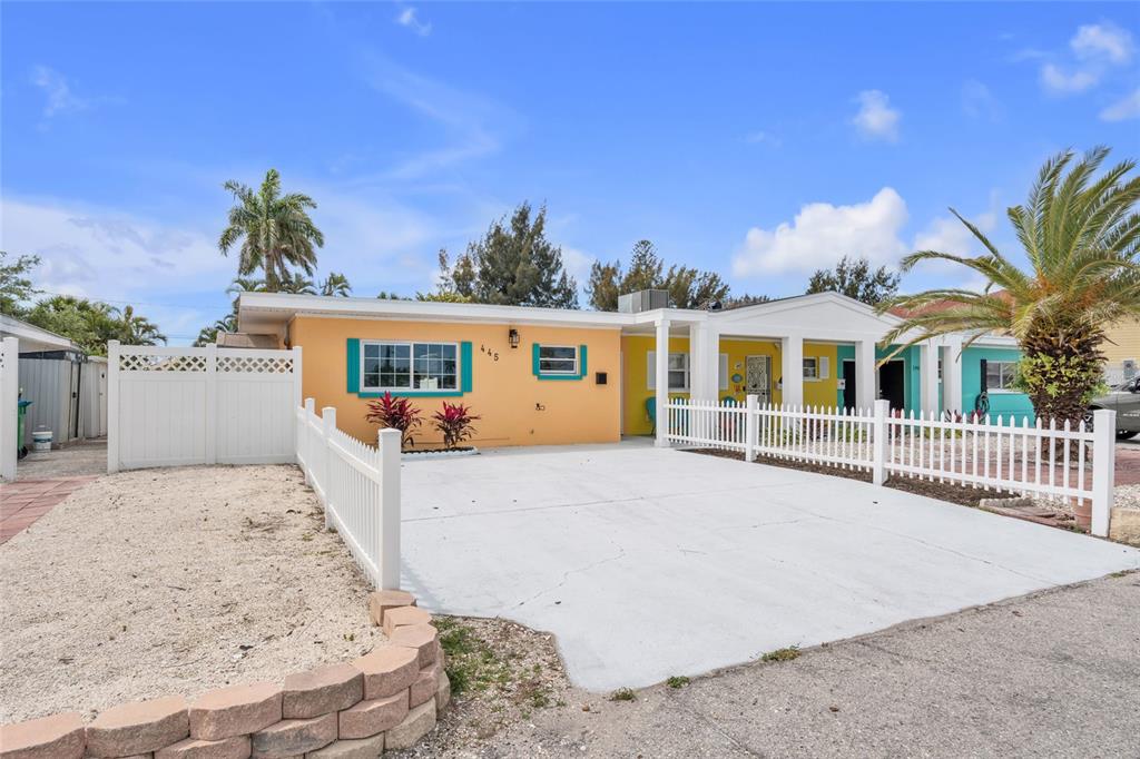 A peach-colored duplex exterior features a white fence, a concrete driveway, and turquoise window trim — 445 63RD STREET, HOLMES BEACH, FL