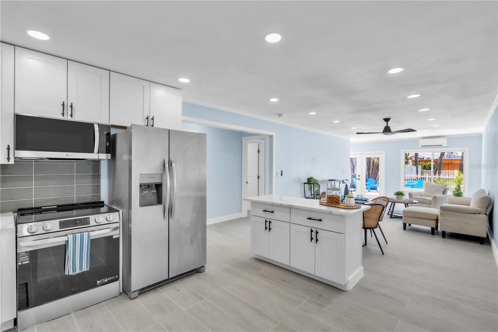 A kitchen with a white island and stainless steel refrigerator opens into a living area — 445 63RD STREET, HOLMES BEACH, FL