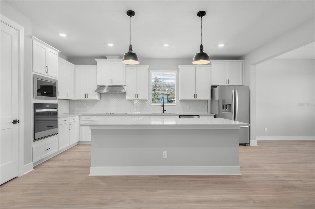 An open-concept living area with light wood-look flooring, a kitchen island, and a ceiling fan — 3849 SADDLE HILL TRAIL, FRUITLAND PARK, FL
