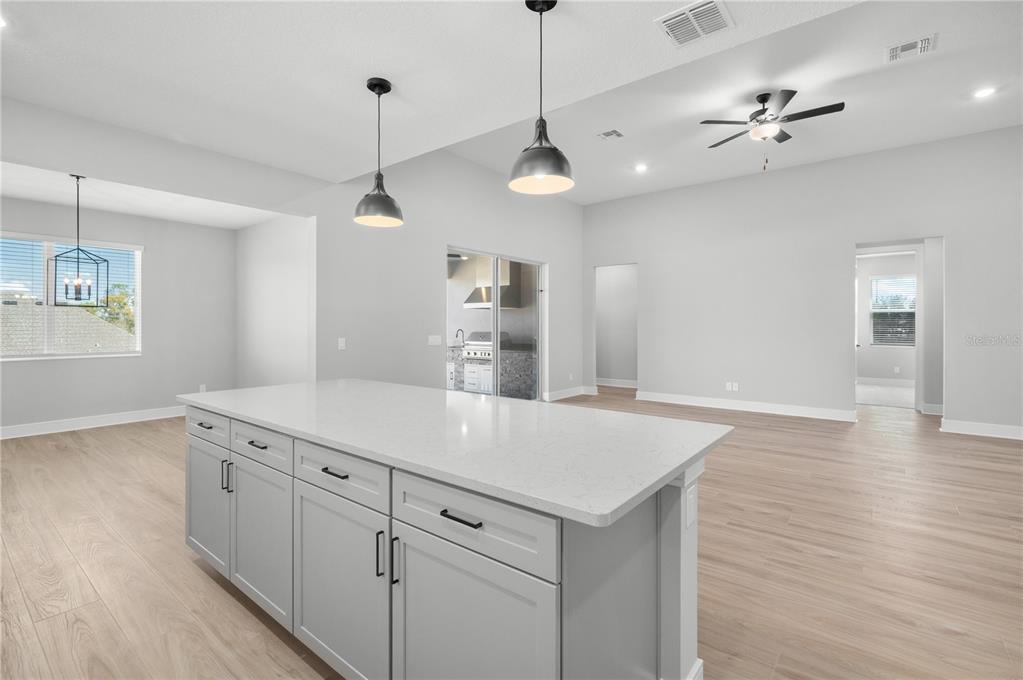 A modern kitchen features white cabinetry, a large central island, stainless steel appliances, and wood flooring — 3849 SADDLE HILL TRAIL, FRUITLAND PARK, FL