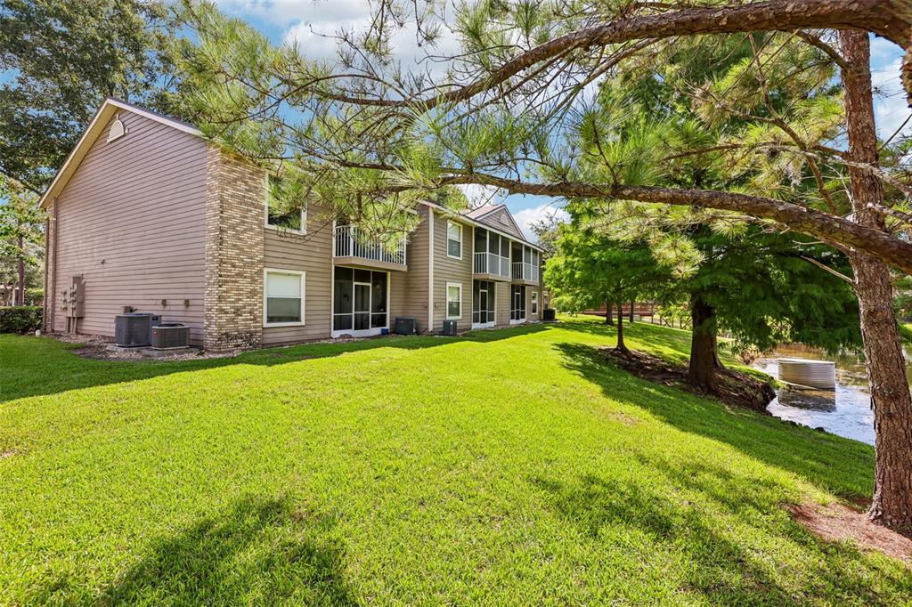 Exterior view of a multi-story apartment building with a grassy lawn and a nearby pond — 124 RESERVE CIRCLE UNIT 100, OVIEDO, FL