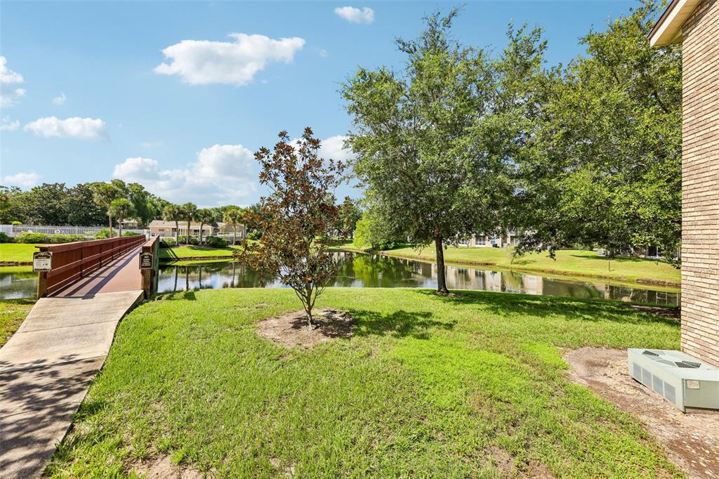 A grassy lawn with trees and a wooden footbridge overlooking a small pond — 124 RESERVE CIRCLE UNIT 100, OVIEDO, FL